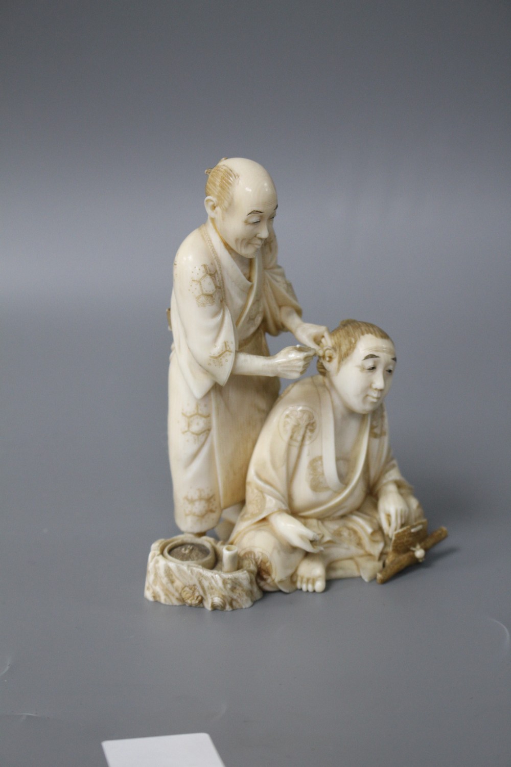 A Japanese Meiji period ivory okimono carved with a doctor treating a mans ear, signed, height 12cm